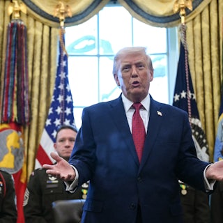 Donald Trump holds his hands out to the side and speaks while standing at his desk in the Oval Office