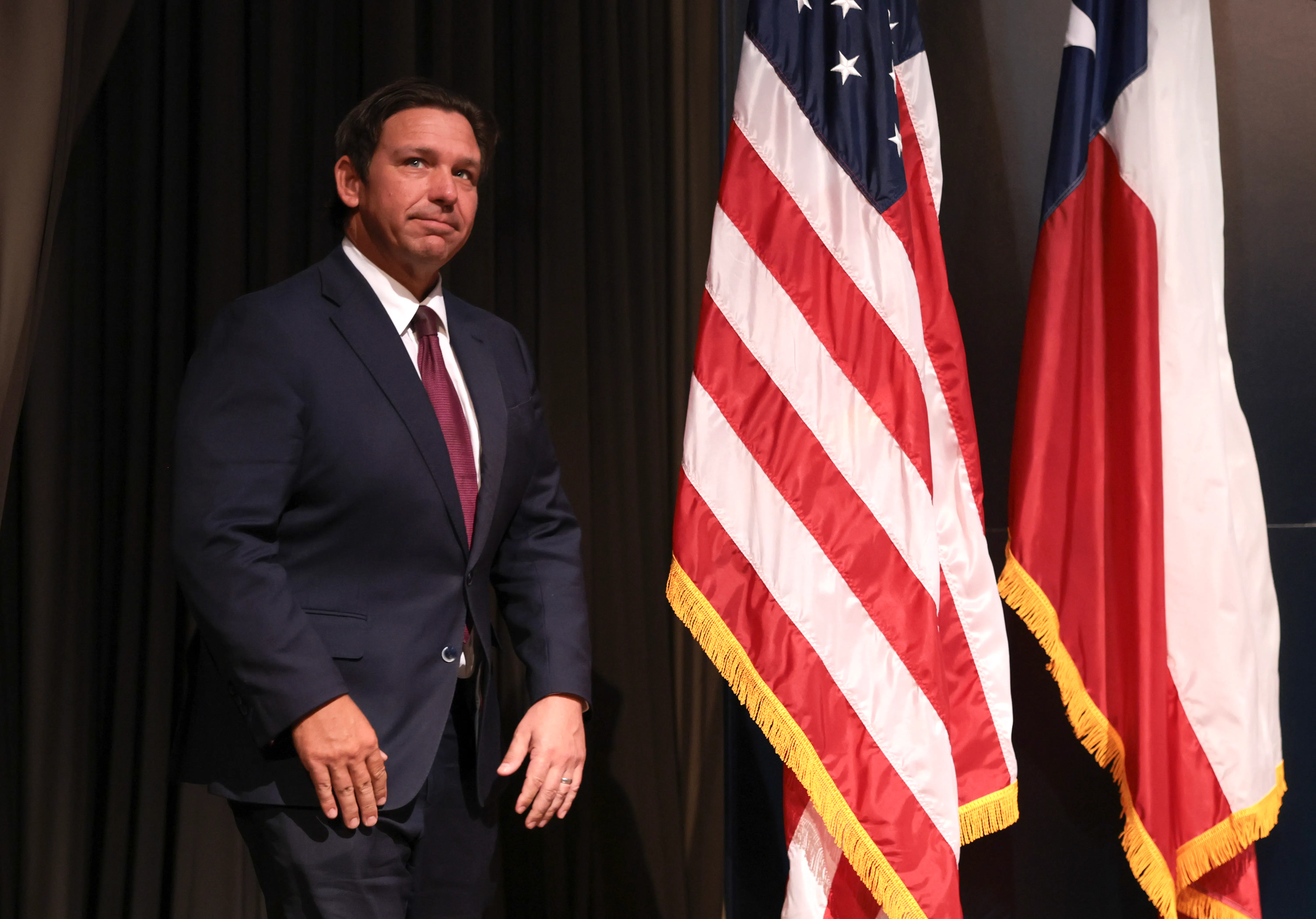 Florida Governor Ron DeSantis stands on stage next to the U.S. and Florida flags.
