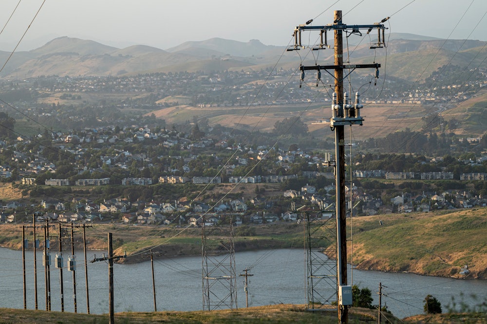Power lines in the foreground are set against a neighborhood of homes on a hillside in the background.