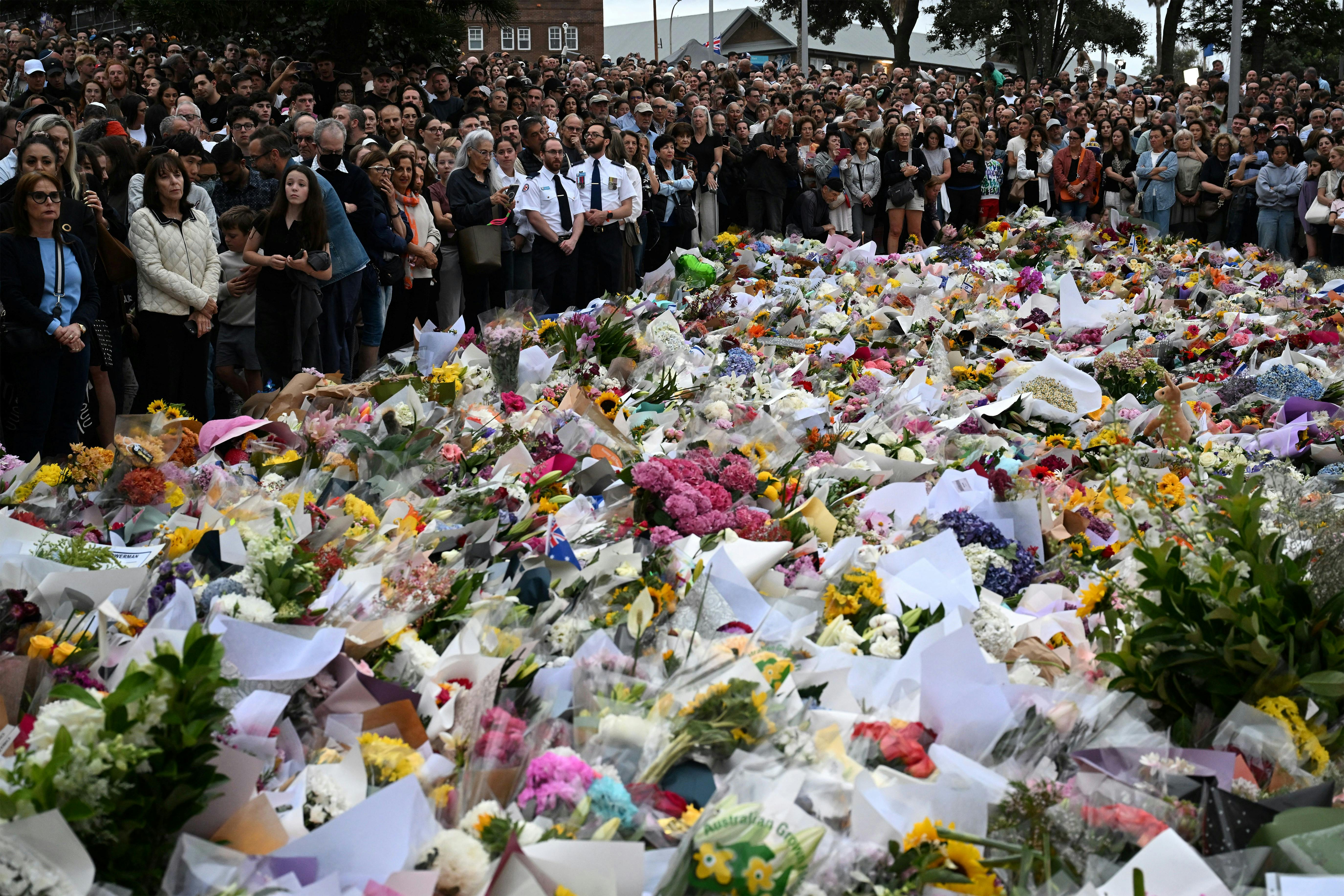 People stand next to a memorial for shooting victims at Bondi Beach