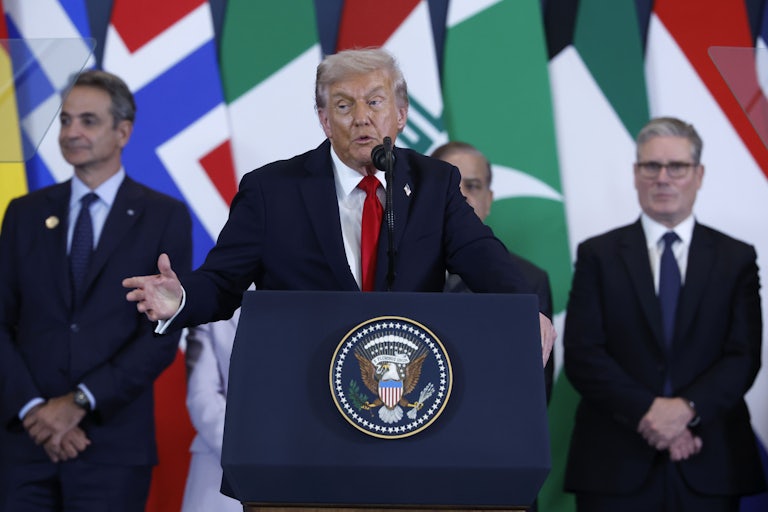 Donald Trump gestures while speaking at a podium while flanked by world leaders