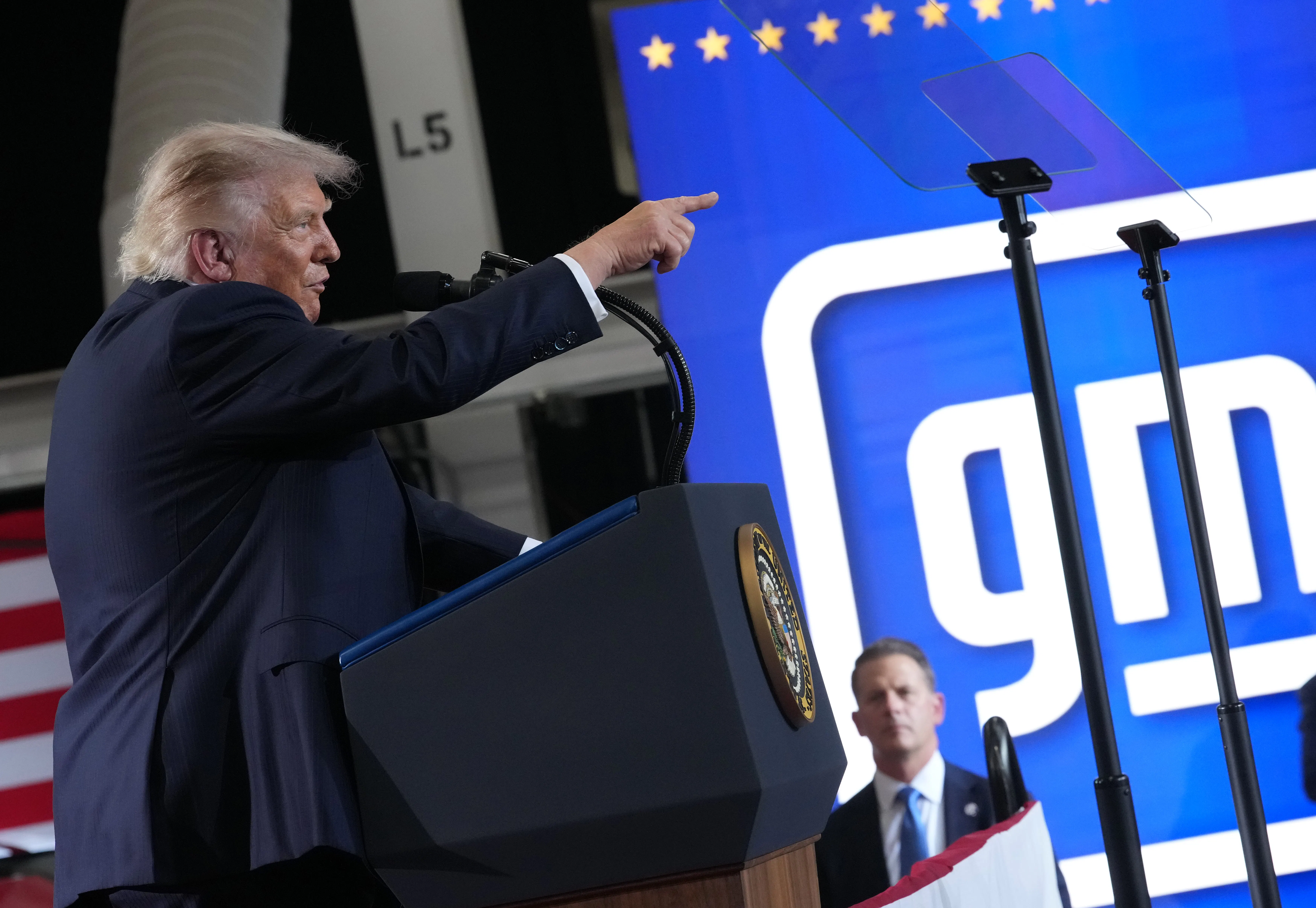 Donald Trump points while speaking behind a podium.