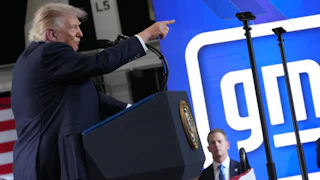 Donald Trump points while speaking behind a podium.