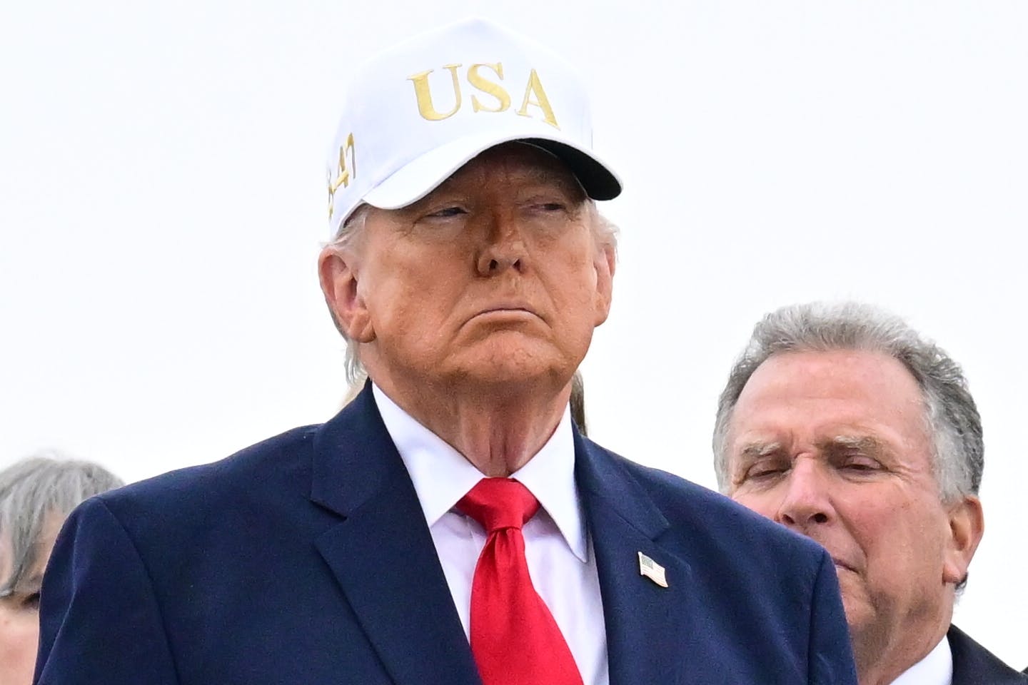 Donald Trump stands while wearing a white "USA" hat