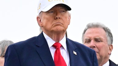 Donald Trump stands while wearing a white "USA" hat
