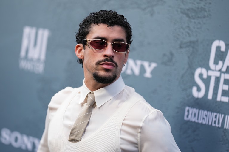 Bad Bunny wears a white shit, white vest, gray tie, and red shades.