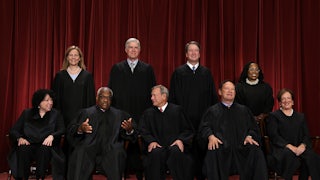 This image shows the nine justices against a red drapery background, with Sotomayor, Thomas, Roberts, Alito, and Kagan sitting, while the others stand behind.