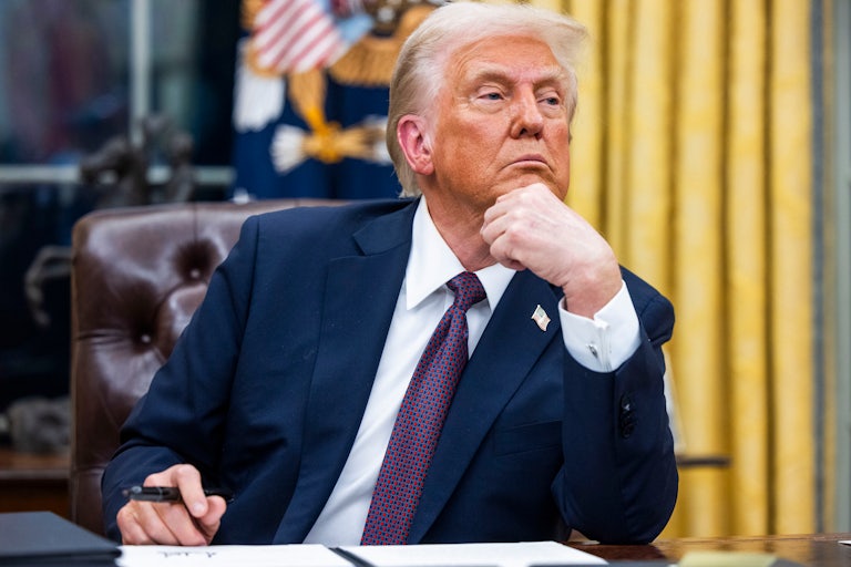 Donald Trump rests his chin on his hand as he signs executive orders in the Oval Office