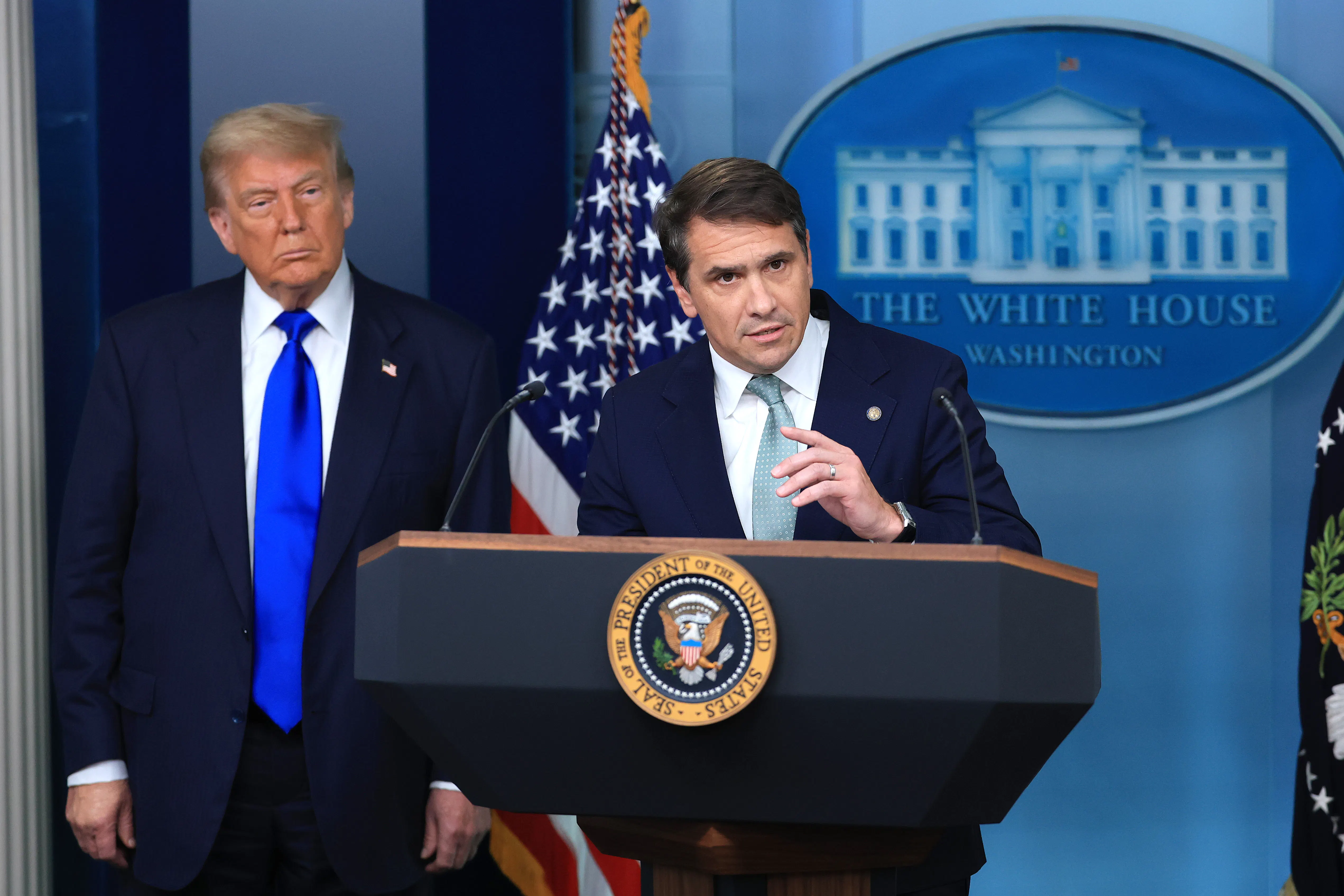 Donald Trump watches as acting Attorney General Todd Blanche speaks at the podium in the White House press briefing room.