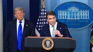 Donald Trump watches as acting Attorney General Todd Blanche speaks at the podium in the White House press briefing room.