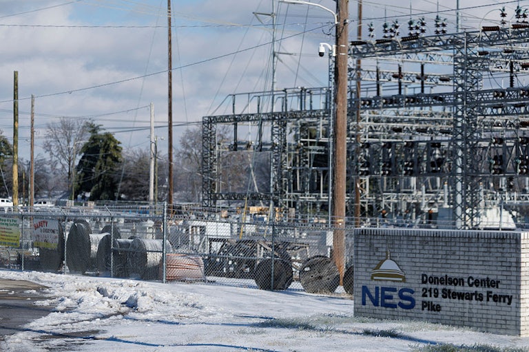 Massive spools of wires, as well as the steel towers of substation, sit behind a chain-link fence, with a sign reading "NES Donelson Center 219 Stewarts Ferry Pike."