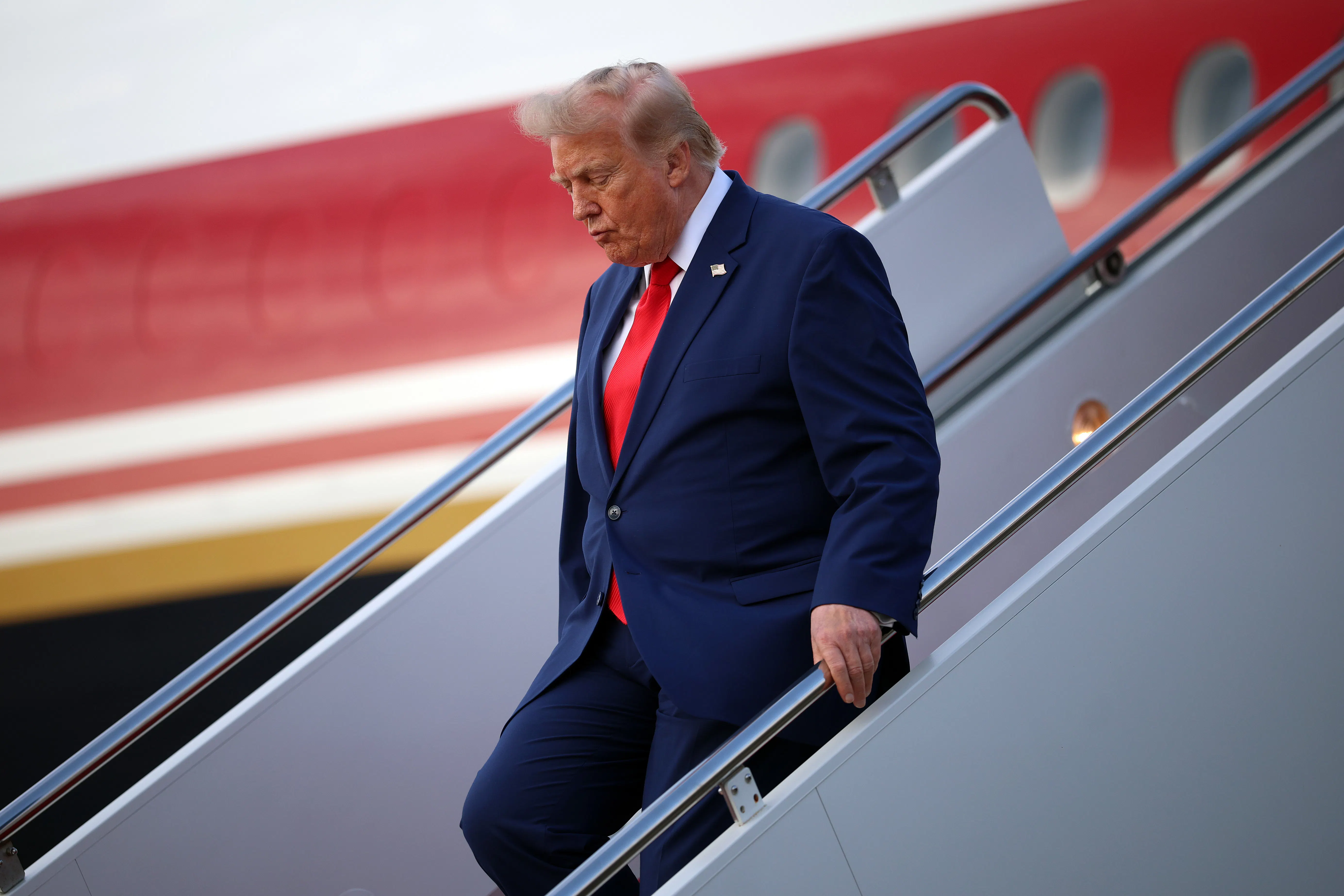 Donald Trump purses his lips and looks down while walking down the steps of Air Force One.