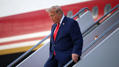 Donald Trump purses his lips and looks down while walking down the steps of Air Force One.
