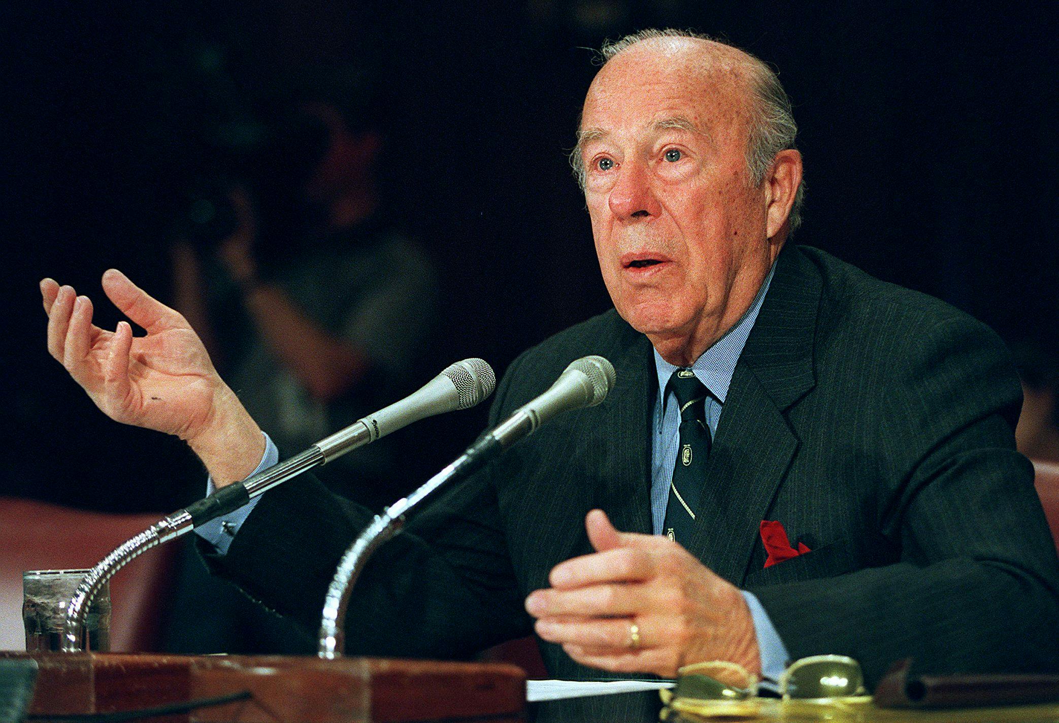George Shultz sits in front of two microphones before the U.S. Senate Foreign Relations Committee in 2000. 