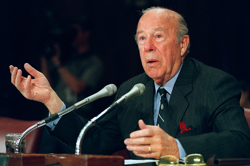George Shultz sits in front of two microphones before the U.S. Senate Foreign Relations Committee in 2000.