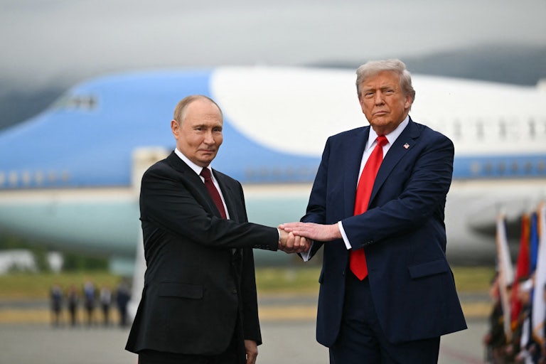 Vladimir Putin and Donald Trump shake hands while standing on a military base tarmac