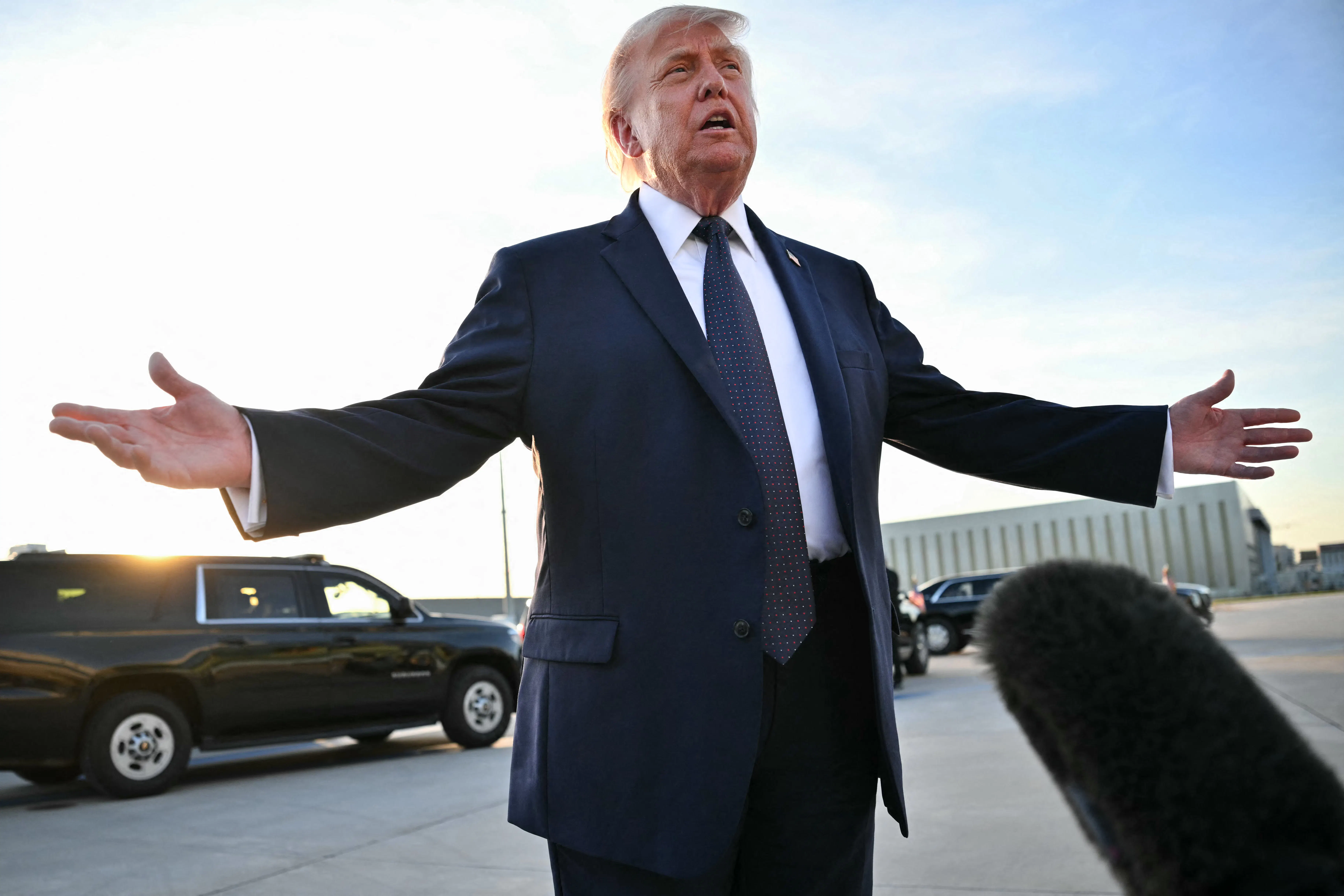 President Donald Trump speaks to reporters on the tarmac and splays his arms outward