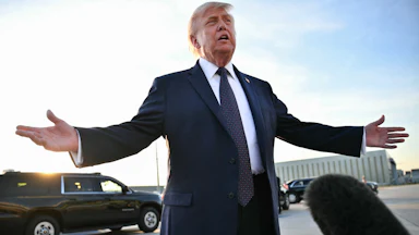 President Donald Trump speaks to reporters on the tarmac and splays his arms outward