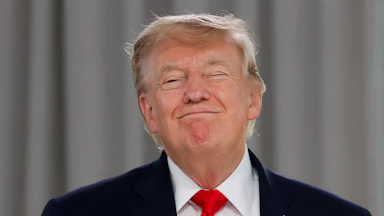 Donald Trump in front a gray curtained background with a triumphant grin, his eyes closed.