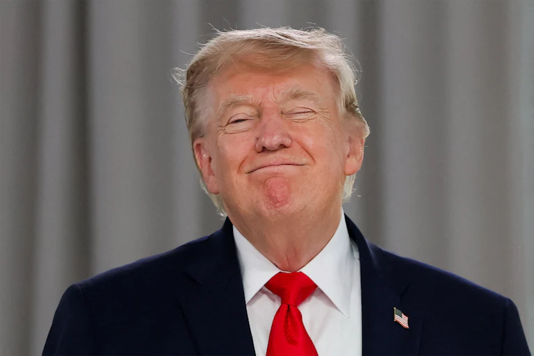 Donald Trump in front a gray curtained background with a triumphant grin, his eyes closed.