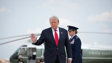 President Donald Trump waves as he leaves Marine One (in the background)