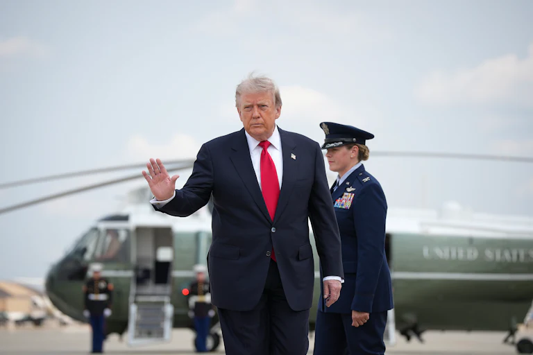 President Donald Trump waves as he leaves Marine One (in the background)