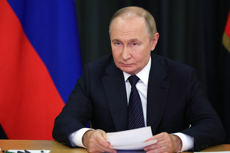 Russian President Vladimir Putin holds a piece of paper while sitting at a table