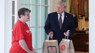 Donald Trump stands outside the Oval Office, holding McDonald's takeout bags while he watches DoorDash driver Sharon Simmons speak