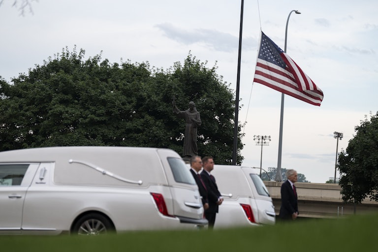 Tree men stand by two white hearses and a U.S. flag being flown at half-mast.