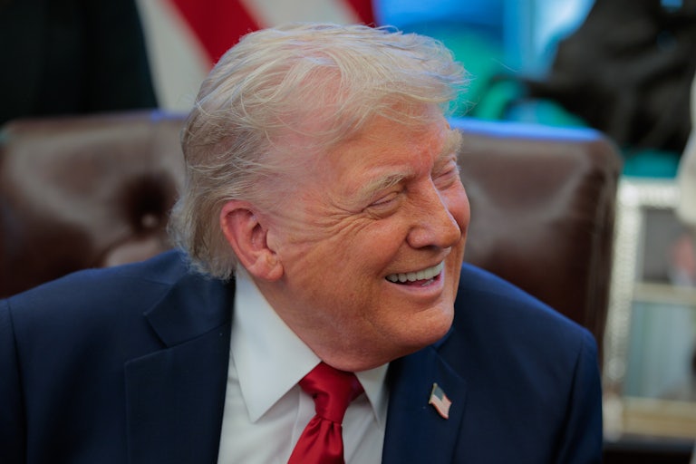 Donald Trump laughs while seated in the Oval Office of the White House.