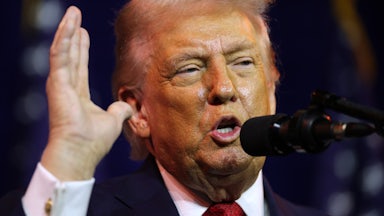 Donald Trump raises his hand while speaking into a microphone