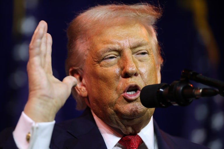 Donald Trump raises his hand while speaking into a microphone