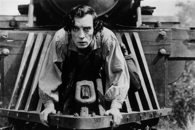 Buster Keaton clings to the front of a train in a black-and-white still