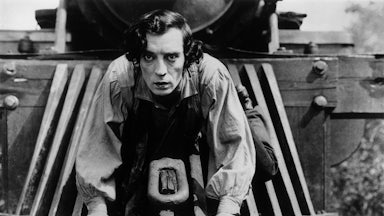 Buster Keaton clings to the front of a train in a black-and-white still