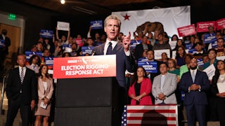 CA Governor Gavin Newsom stands in front of a crowd at a podium.