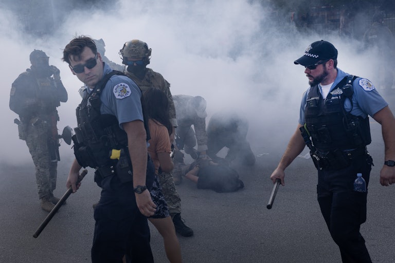 Chicago police officers holding batonsn walk through tear gas.