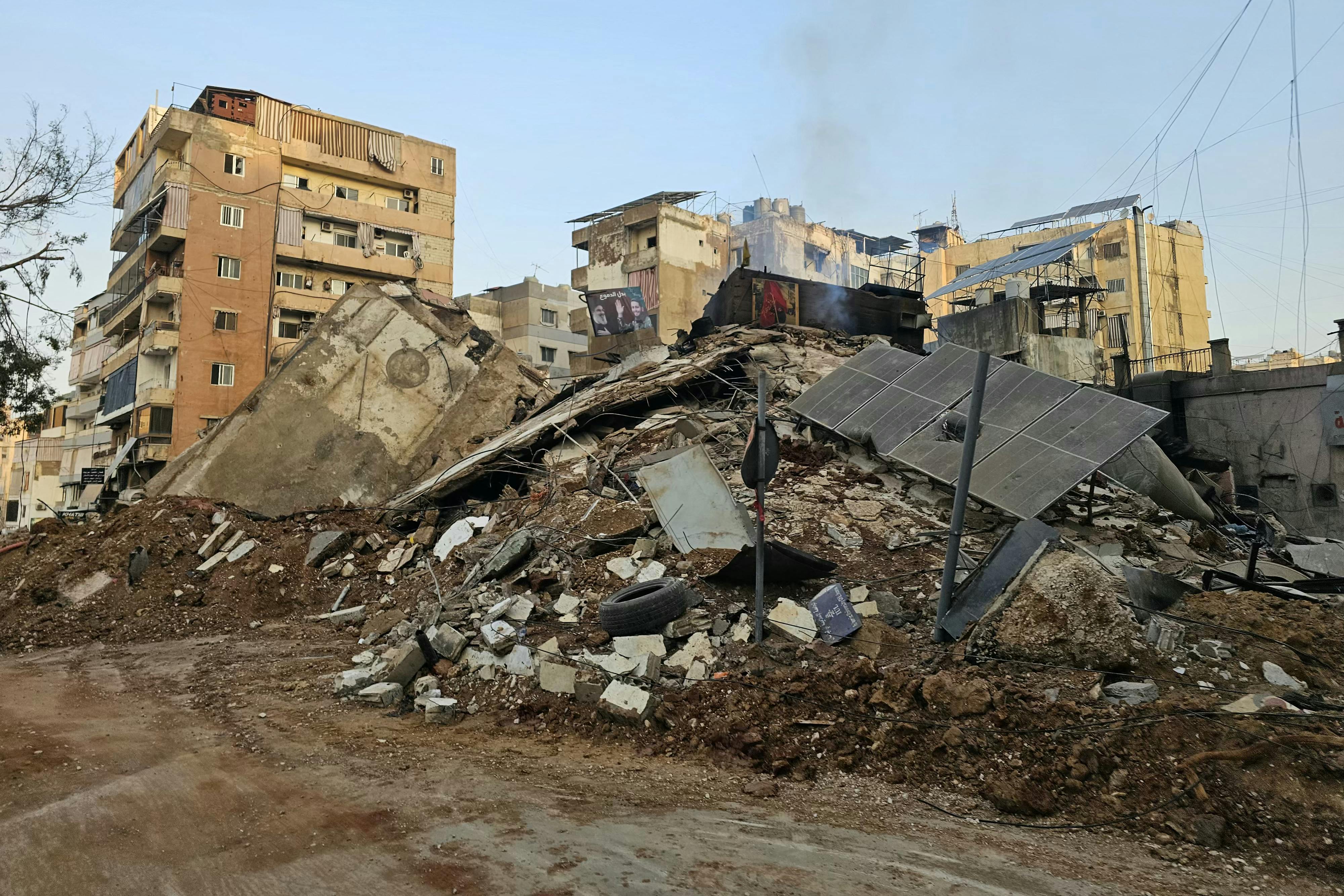 Solar panels lie on a pile of rubble next to other damaged buildings.