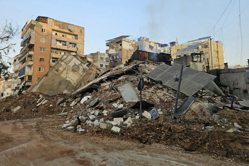 Solar panels lie on a pile of rubble next to other damaged buildings.