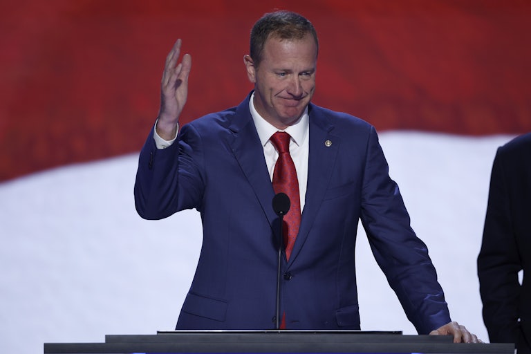 Eric Schmitt speaks and waves in front of a large U.S. flag.