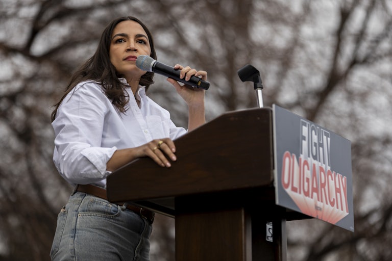 Representative Alexandria Ocasio-Cortez speaks at a lectern that reads "Fight Oligarchy."