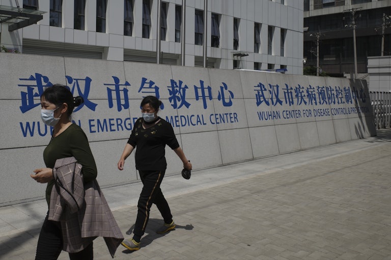 People walk past a building labeled “Wuhan Emergency Medical Center” and “Wuhan Center for Disease Control and Prevention.”