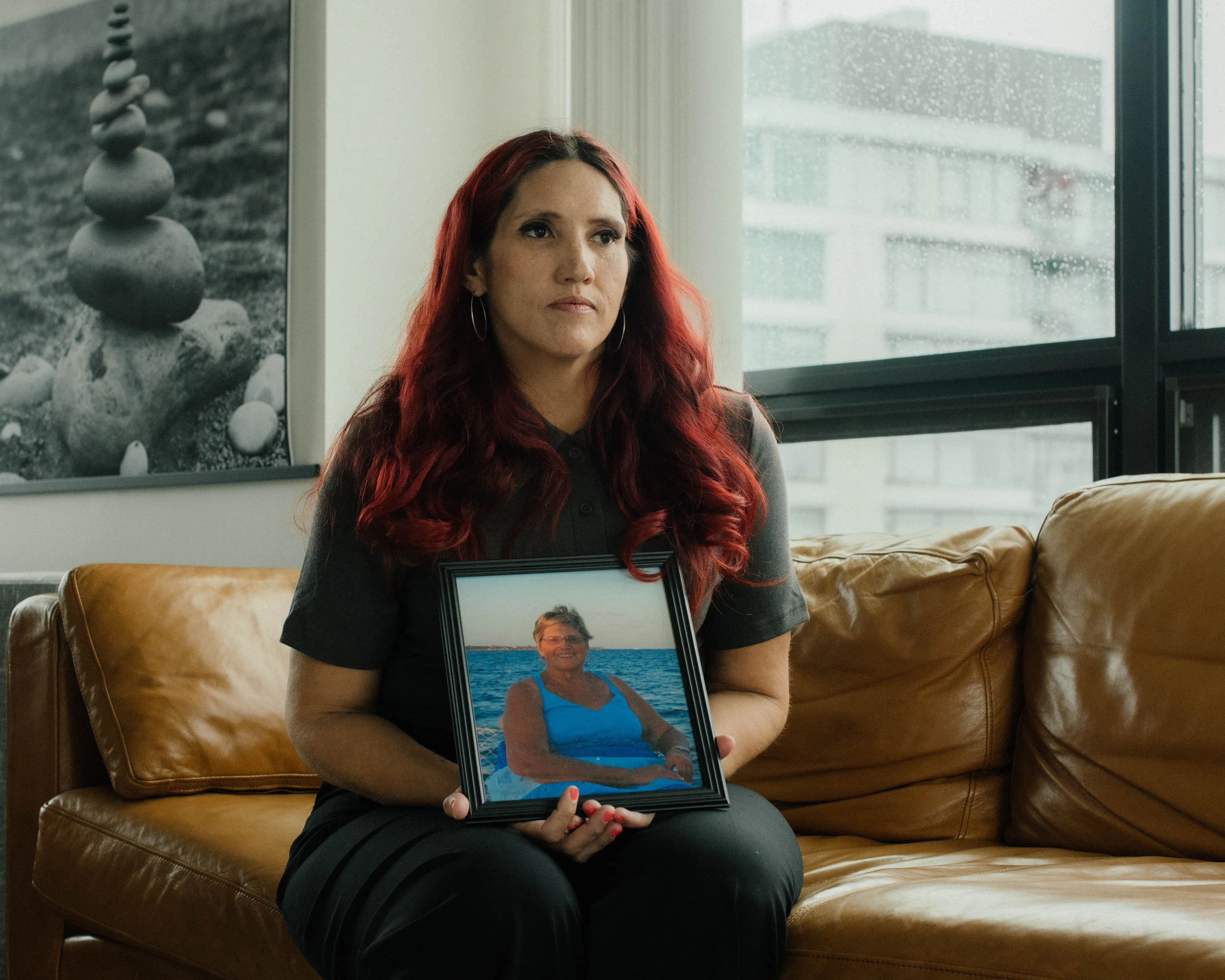 A portrait of Misty Leon holding a photograph of her mother, sitting on a couch in an apartment in Vancouver, Canada.
