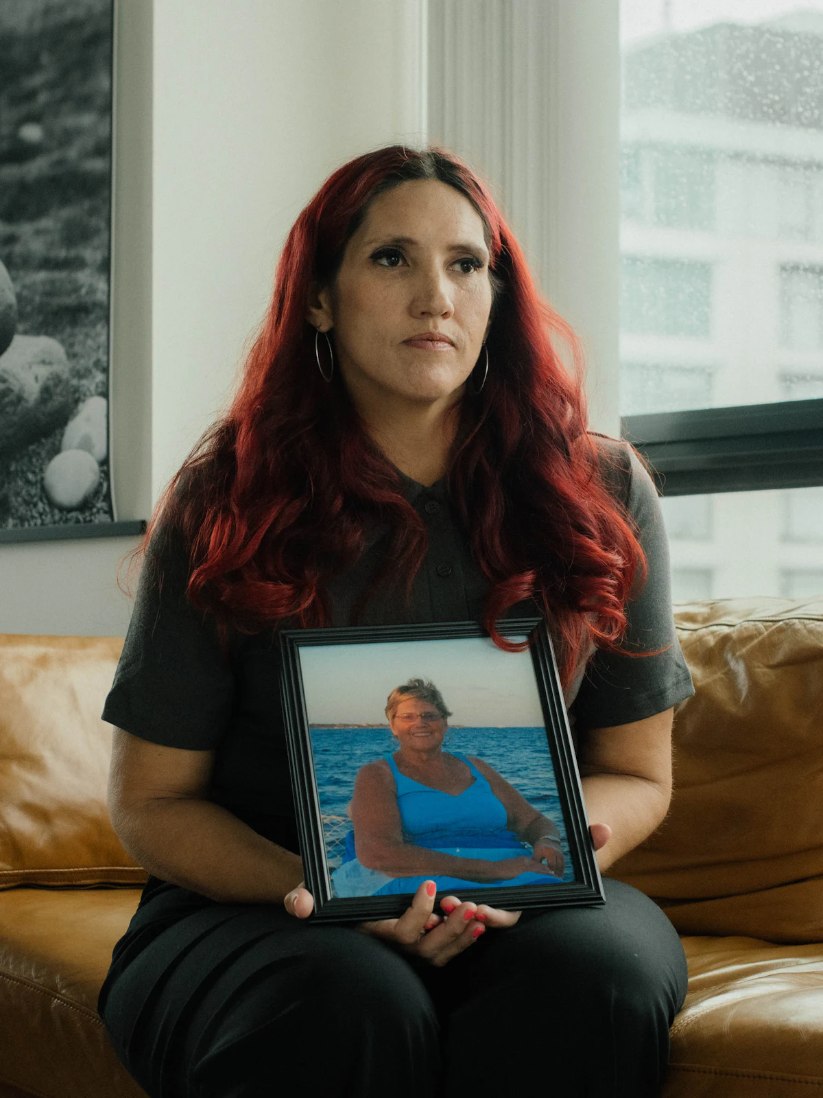 A portrait of Misty Leon holding a photograph of her mother, sitting on a couch in an apartment in Vancouver, Canada.