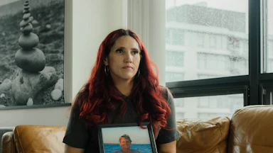 A portrait of Misty Leon holding a photograph of her mother, sitting on a couch in an apartment in Vancouver, Canada.