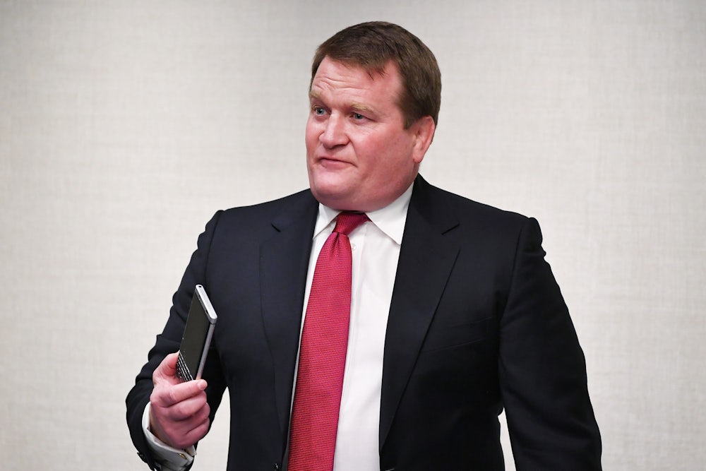 Tony Bobulinski, wearing a suit, looks off camera and holds a phone in his hand.
