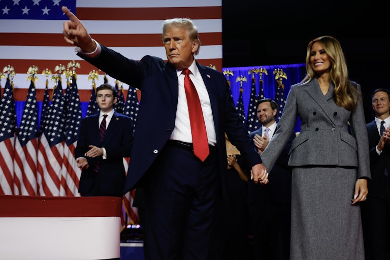 Donald Trump points to the crowd as Melania Trump holds his hand and smiles