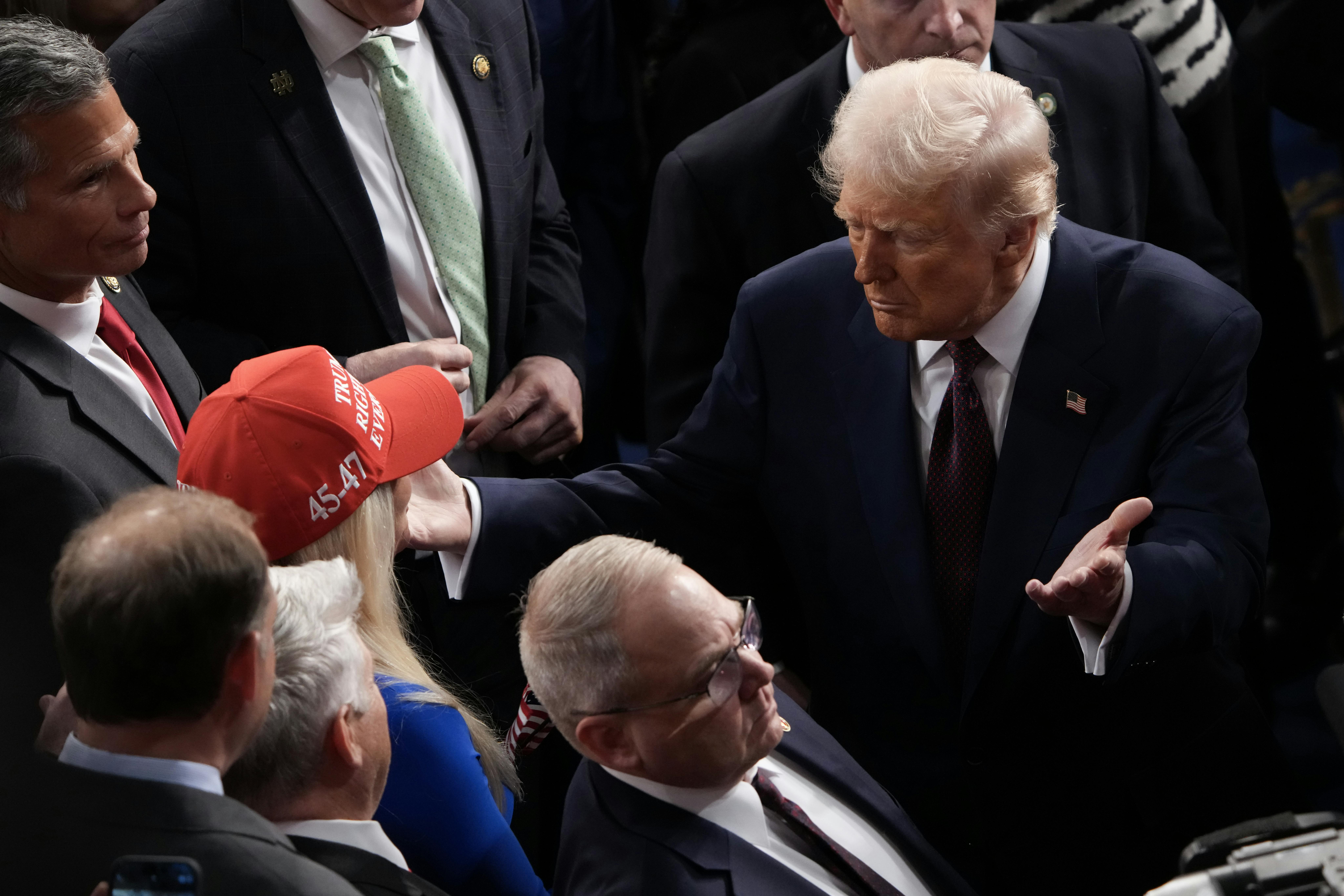 Donald Trump moves through a crowd to hug Marjorie Taylor Greene, who wears a red "Trump Was Right About Everything" cap.