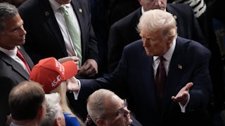 Donald Trump moves through a crowd to hug Marjorie Taylor Greene, who wears a red "Trump Was Right About Everything" cap.
