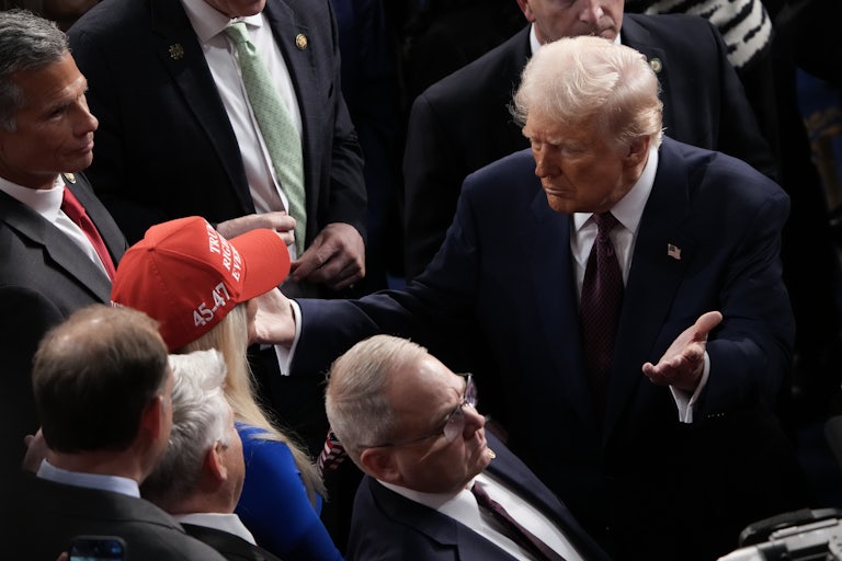 Donald Trump moves through a crowd to hug Marjorie Taylor Greene, who wears a red "Trump Was Right About Everything" cap.