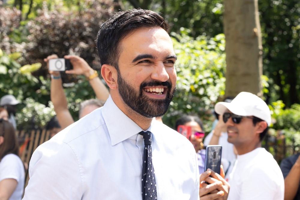 New York City mayoral candidate Zohran Mamdani is seen at the 2025 NYC Pride March on June 29, 2025 in New York, New York. He is wearing a white button-up shirt and a spotted black tie and smiling.